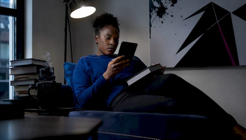 Woman comparing e-reader and paperback in cozy living room