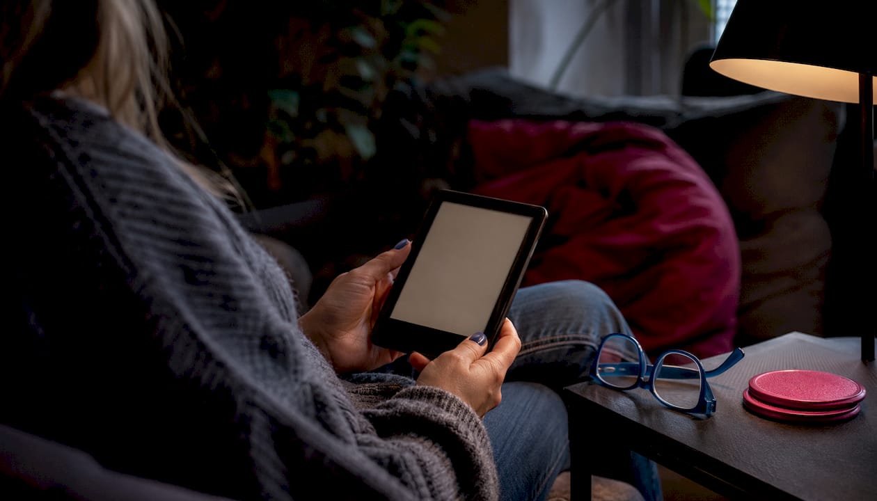 Overhead view of hands holding Kobo e-reader at desk workspace