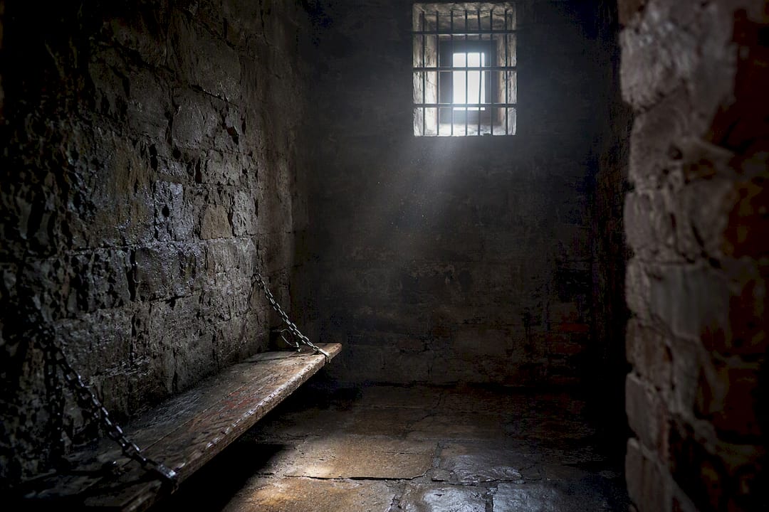 Dim prison cell corner with bench and shadows