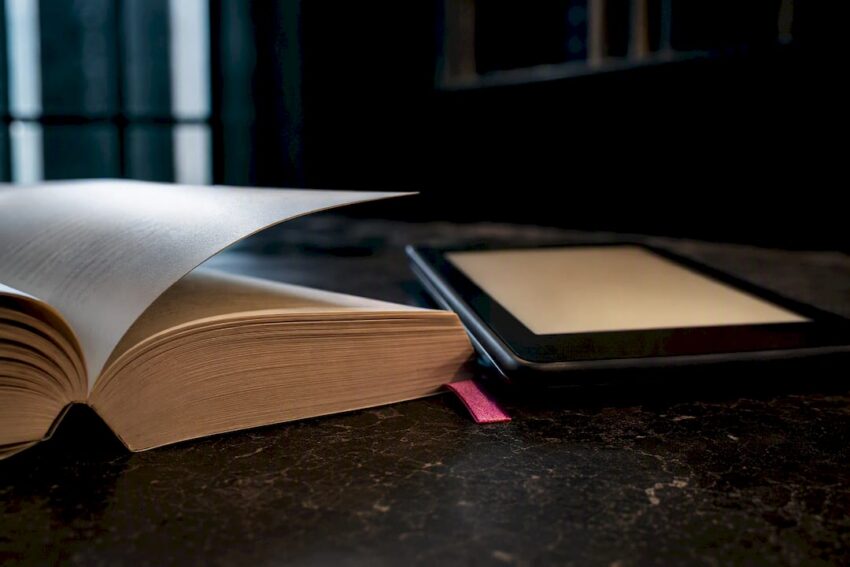 Cropped paperback beside anonymous e-reader